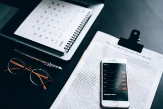 Ilustrasi: Ponsel pintar dengan aplikasi pasar saham di atas dokumen bersama kacamata dan kalender meja.