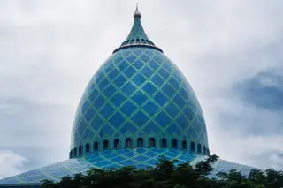 Ilustrasi: Kubah masjid bercorak geometris biru dan hijau dengan latar langit berawan.