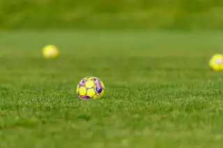 Ilustrasi: Bola sepak berwarna kuning bermotif tergeletak di atas lapangan rumput hijau.