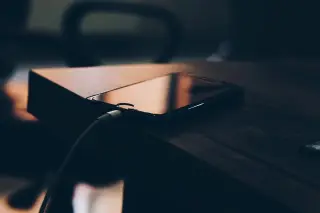 Ilustrasi: Sebuah ponsel pintar terhubung kabel pengisi daya tergeletak di atas meja kayu.