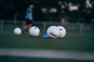 Ilustrasi: Bola sepak putih di atas rumput lapangan dengan sosok buram di latar belakang.