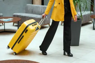 Ilustrasi: Seseorang berjas kuning menarik koper berwarna kuning di dalam lobi.