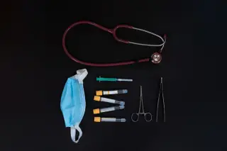 Ilustrasi: Peralatan medis seperti stetoskop, masker, tabung sampel, dan jarum suntik di atas latar belakang hitam.