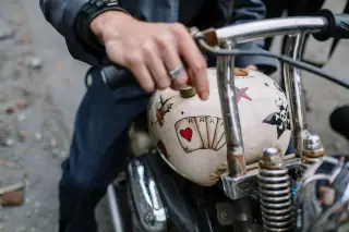 Ilustrasi: Tangan seseorang memegang stang sepeda motor kustom dengan tangki bergambar kartu remi.