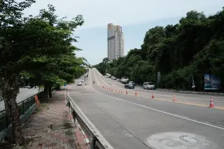 Ilustrasi: Jalan raya beraspal dengan deretan kerucut lalu lintas menuju gedung tinggi di kejauhan.