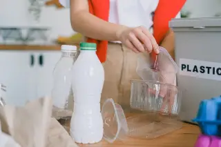 Ilustrasi: Seseorang memilah botol dan wadah plastik daur ulang ke dalam tempat sampah bertuliskan plastik.