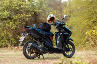 Ilustrasi: Sepeda motor matik hitam terparkir di area terbuka dengan helm dan tas di atasnya.