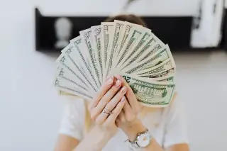 Ilustrasi: Seseorang memegang kipasan uang kertas dolar Amerika Serikat di depan wajahnya.