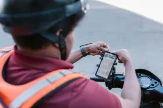 Ilustrasi: Seorang pengendara motor berhelm memasang ponsel pintar dengan peta digital di stang kemudi.