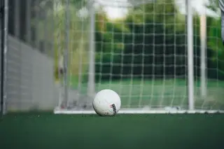 Ilustrasi: Sebuah bola sepak putih tergeletak di rumput dekat jaring gawang.