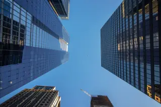Ilustrasi: Sudut pandang rendah gedung-gedung pencakar langit modern berlatar langit biru cerah.