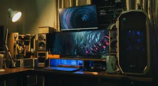 Ilustrasi: Meja kerja dengan komputer desktop, monitor ganda, speaker, dan lampu meja.