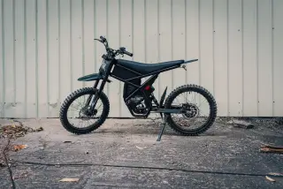 Ilustrasi: Sepeda motor listrik bergaya trail warna hitam terparkir di depan dinding seng.