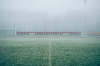 Ilustrasi: Lapangan sepak bola kosong dan deretan kursi tribun yang diselimuti kabut tebal.