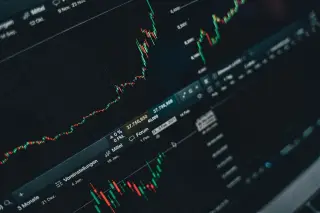 Ilustrasi: Layar monitor menampilkan grafik pergerakan harga saham dan data pasar keuangan berlatar gelap.