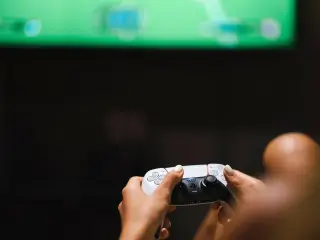Ilustrasi: Seseorang memegang pengontrol permainan video nirkabel di depan layar televisi.