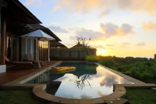 Ilustrasi: Kolam renang di sebuah vila dengan latar langit senja dan pepohonan hijau.
