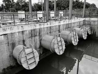 Ilustrasi: Foto hitam-putih deretan pipa saluran air industri besar dengan katup pembuangan.