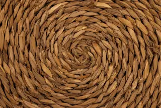 Ilustrasi: Pola spiral anyaman serat alami berwarna cokelat yang terjalin rapat.