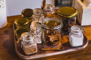 Ilustrasi: Aneka toples kaca berisi rempah-rempah dan bahan dapur di atas nampan kayu.