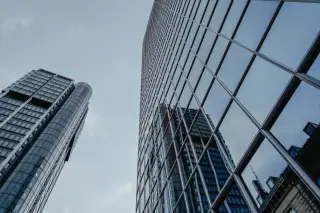 Ilustrasi: Gedung pencakar langit modern berdinding kaca dipotret dari sudut rendah berlatar langit.