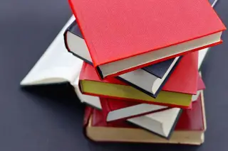 Ilustrasi: Tumpukan buku tebal bersampul warna-warni di atas permukaan gelap.