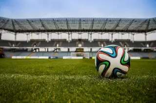 Ilustrasi: Sebuah bola sepak tergeletak di atas rumput lapangan dengan latar belakang tribun stadion.