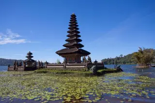 Ilustrasi: Pura Ulun Danu Beratan bertingkat di tepi danau yang tenang di bawah langit biru cerah.