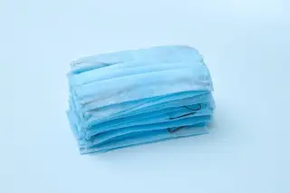 Ilustrasi: Tumpukan masker medis sekali pakai berwarna biru di atas latar belakang biru muda.