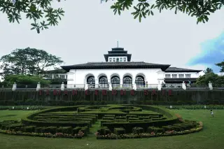 Ilustrasi: Pemandangan Gedung Sate dengan taman hijau berundak di depannya.