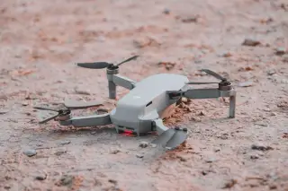 Ilustrasi: Sebuah drone kecil berwarna abu-abu terparkir di atas tanah berbatu.