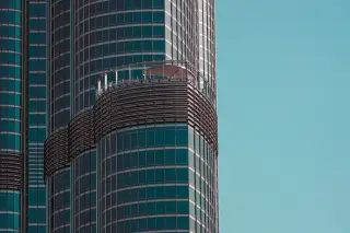 Ilustrasi: Fasad kaca modern sebuah gedung pencakar langit dengan latar belakang langit biru cerah.