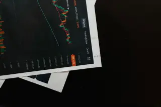 Ilustrasi: Cetakan kertas berisi grafik pergerakan saham di atas permukaan hitam.