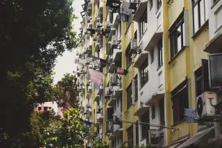Ilustrasi: Fasad bangunan apartemen bertingkat dengan jemuran pakaian dan deretan unit pendingin udara.