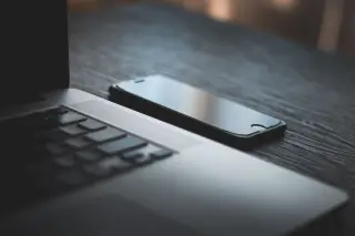 Ilustrasi: Sebuah laptop dan ponsel pintar diletakkan di atas meja kayu gelap.