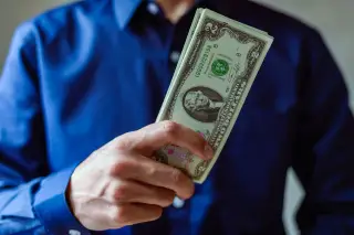 Ilustrasi: Seseorang berkemeja biru memegang segepok uang kertas dolar Amerika Serikat.