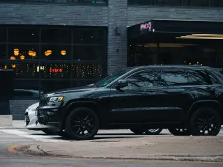Ilustrasi: Mobil SUV berwarna hitam terparkir di pinggir jalan depan bangunan modern.