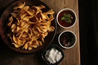 Ilustrasi: Semangkuk keripik renyah dan mangkuk-mangkuk kecil saus serta bumbu di atas meja kayu.