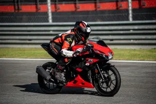 Ilustrasi: Seorang pengendara motor balap berbaju pelindung melaju di lintasan sirkuit aspal.