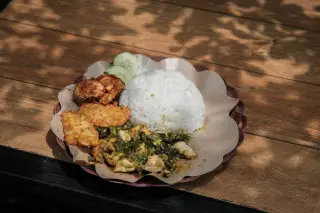 Ilustrasi: Seporsi nasi putih dengan olahan ayam geprek, tempe goreng, dan timun di atas meja kayu.