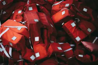Ilustrasi: Tumpukan pelampung keselamatan berwarna oranye dan merah dengan pita reflektif putih.