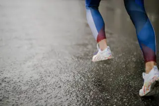 Ilustrasi: Kaki seorang pelari mengenakan celana ketat biru dan sepatu kets melangkah di jalan aspal basah.