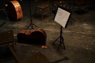 Ilustrasi: Alat musik selo dan partitur tergeletak di panggung orkestra yang kosong.