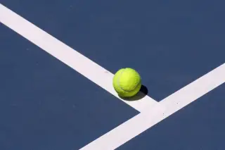 Ilustrasi: Sebuah bola tenis kuning berada di atas garis putih lapangan tenis biru.