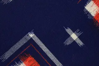Ilustrasi: Foto jarak dekat kain tenun berwarna biru tua dengan pola geometris putih dan oranye.