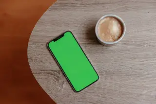 Ilustrasi: Ponsel pintar dengan layar hijau dan secangkir kopi di atas meja kayu.