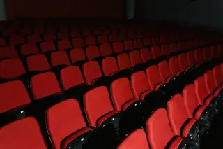 Ilustrasi: Deretan kursi merah kosong di dalam ruangan bioskop yang gelap.