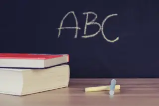 Ilustrasi: Buku dan kapur di atas meja kayu di depan papan tulis bertuliskan ABC.