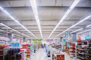 Ilustrasi: Lorong supermarket modern dengan deretan rak barang di bawah lampu plafon yang terang.