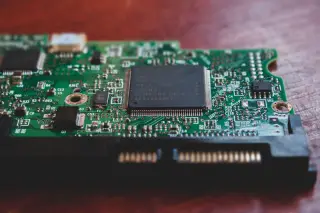 Ilustrasi: Papan sirkuit elektronik hijau dengan chip mikroprosesor di atas meja kayu.